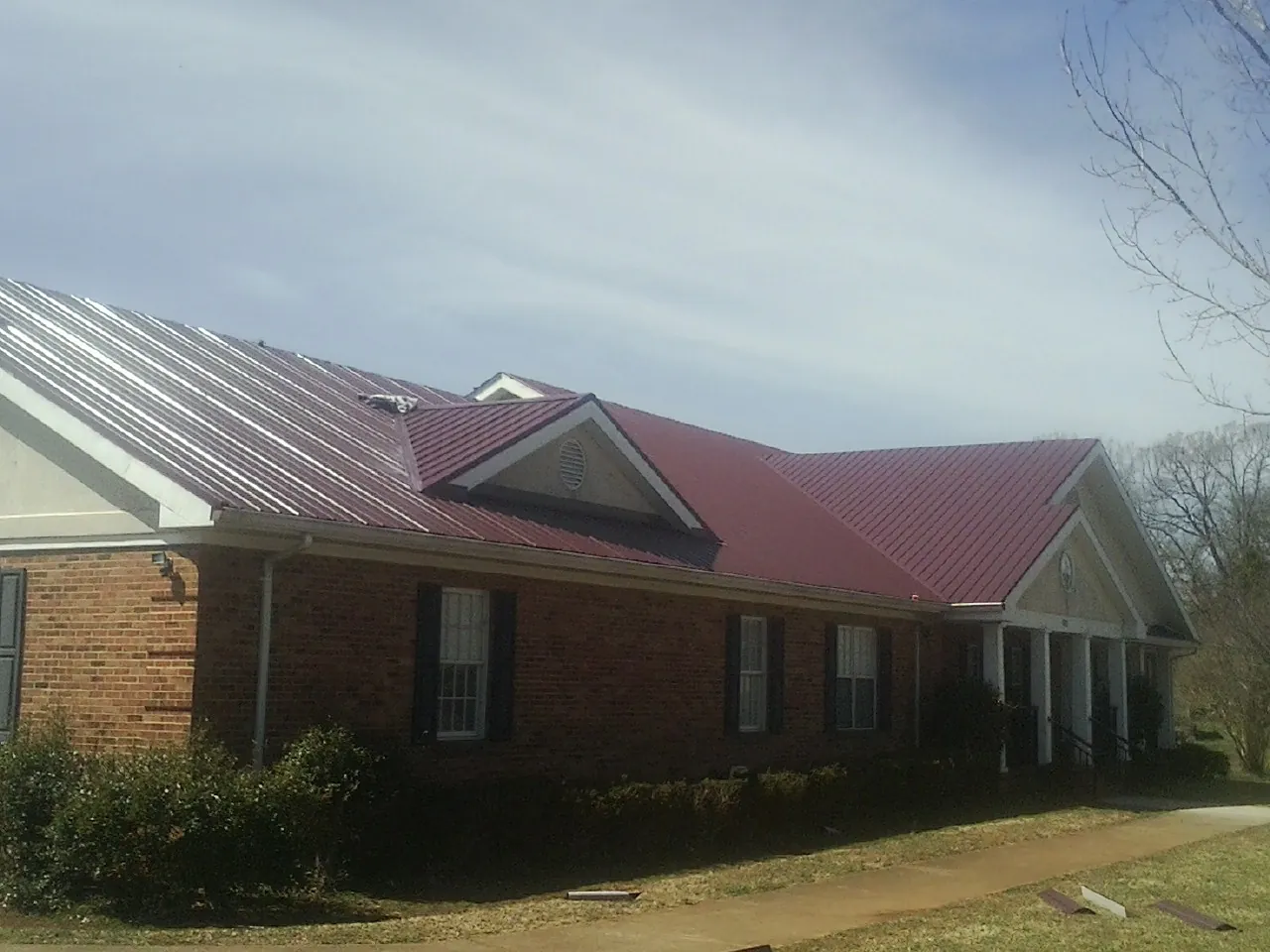 Red metal roof with gabled entries on a long brick building, from a Hail Damage Roof Repair job in Sandy Hook