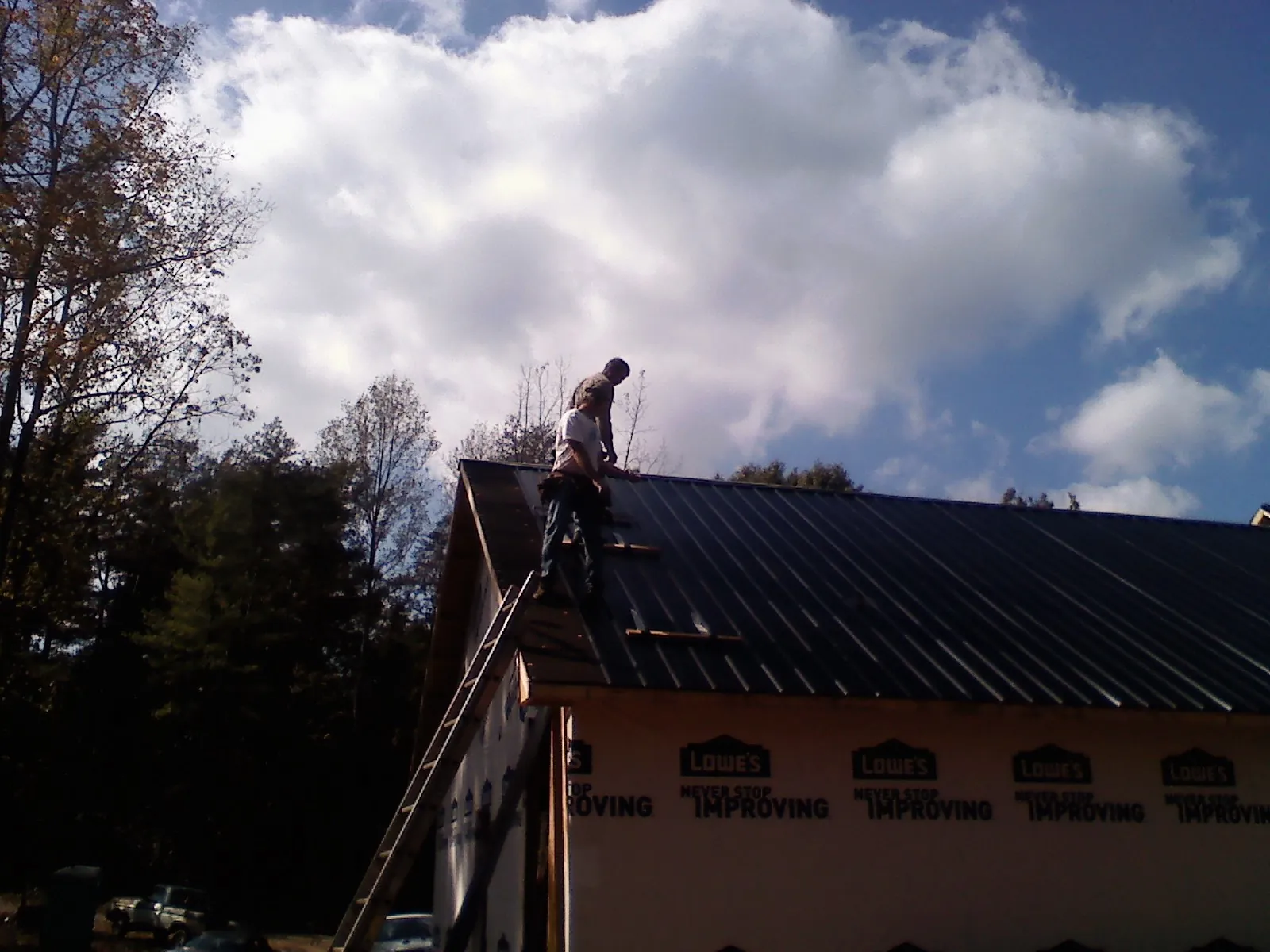 Roofer fastening dark metal panels high against a cloudy sky, from a Roof Inspection job in Sandy Hook